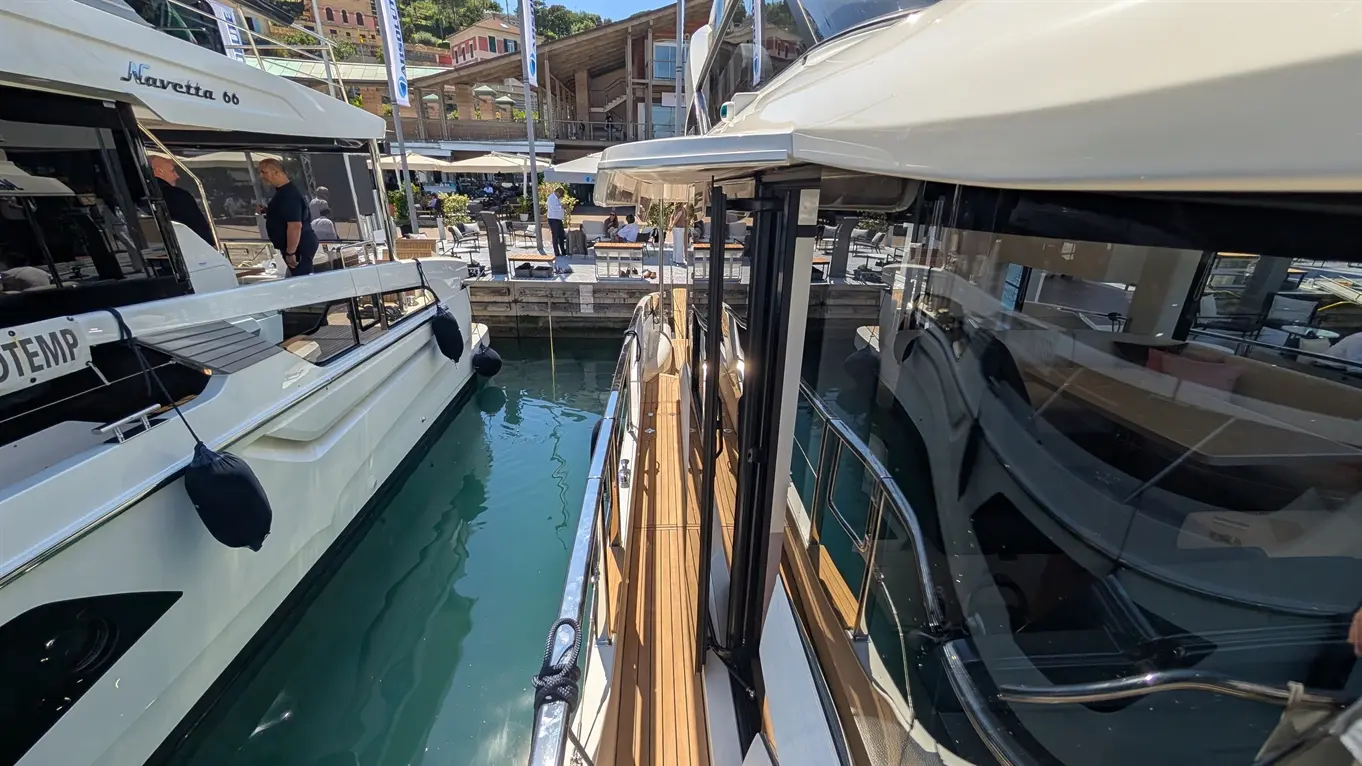 A Navetta 66 yacht docked at a marina, with people dining at nearby tables and clear blue water reflecting sunlight.
